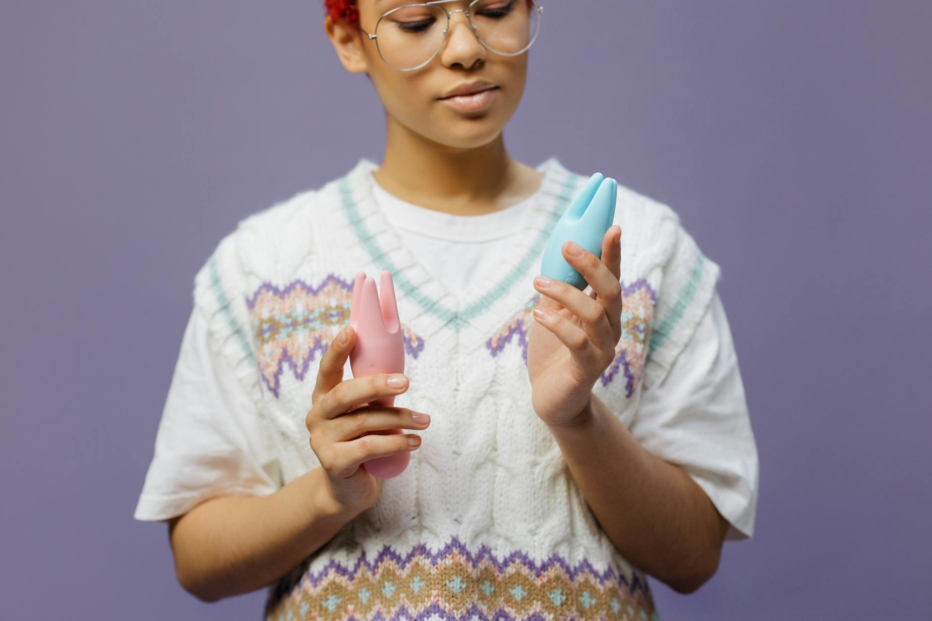 Woman thoughtfully holding blue and pink silicone vibrators, representing the vulnerability of introducing pleasure tools to a new partner.