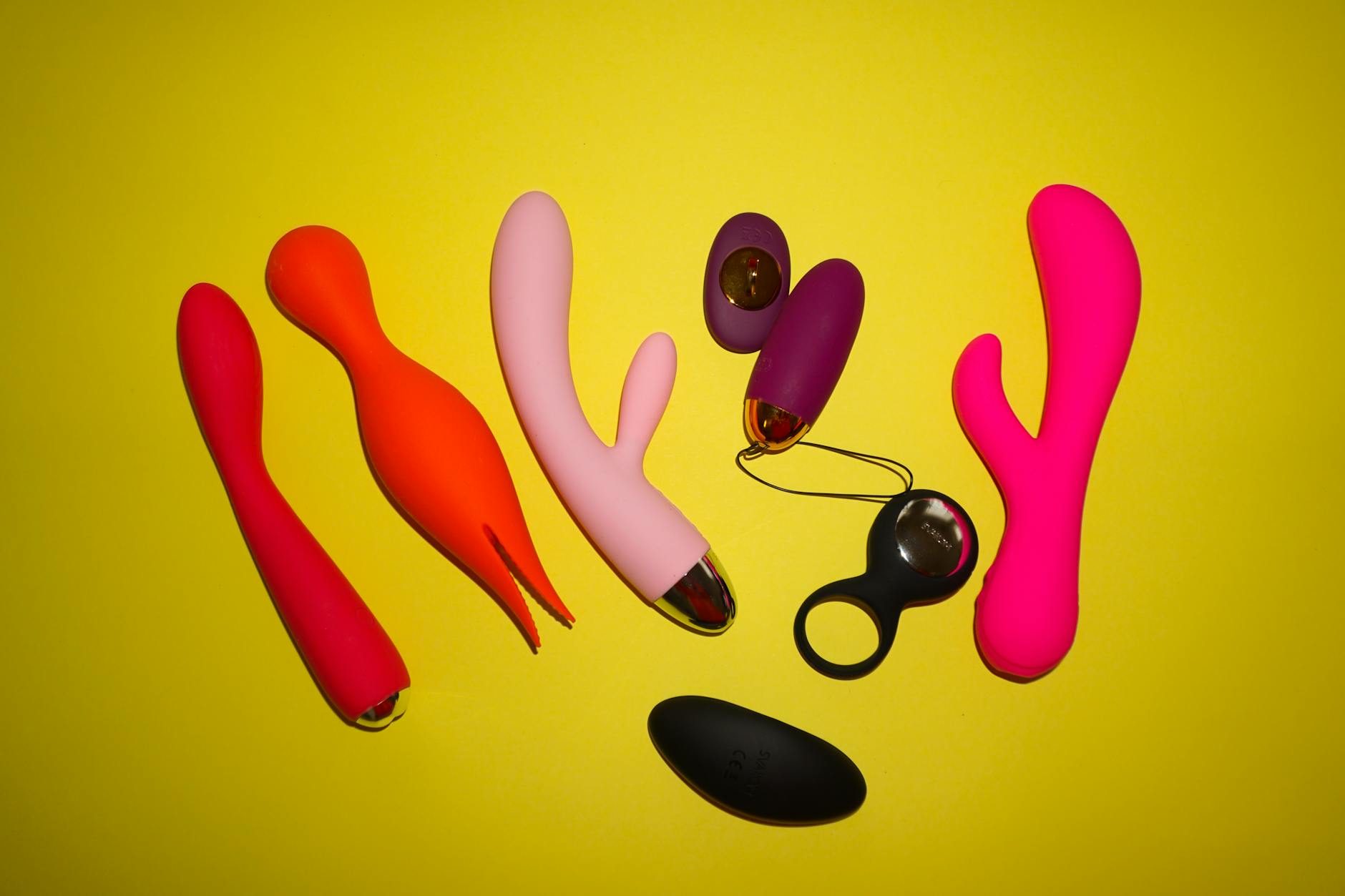 Colorful clitoral vibrators arranged on a bright yellow background, showcasing different toy designs